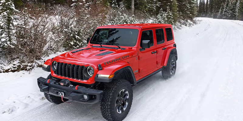 A red Jeep Wrangler Rubicon driving on a snowy road through a forest.