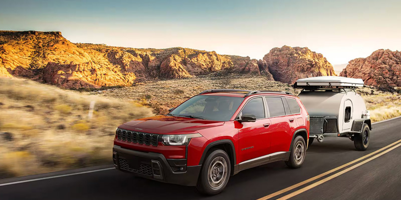 A red SUV towing a small trailer on a scenic road.