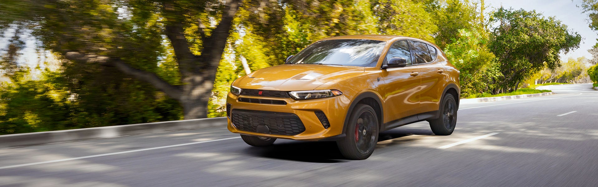 A bright yellow Dodge Hornet drives down a sunny road