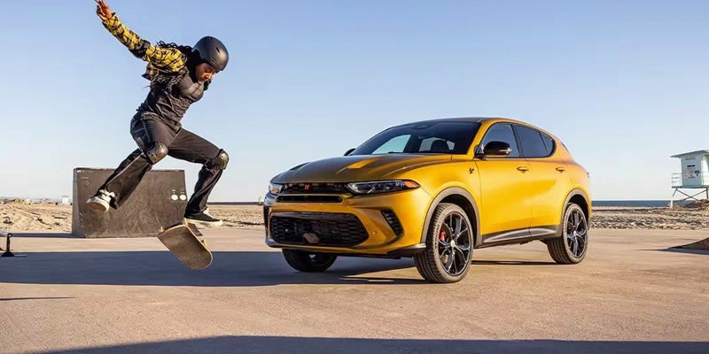 A skateboarder does a trick near a yellow SUV Dodge Hornet