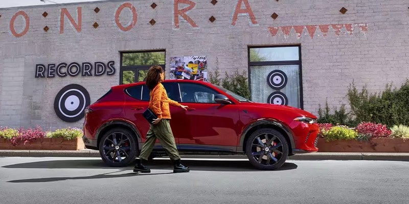 A person stands next to a red SUV in a city