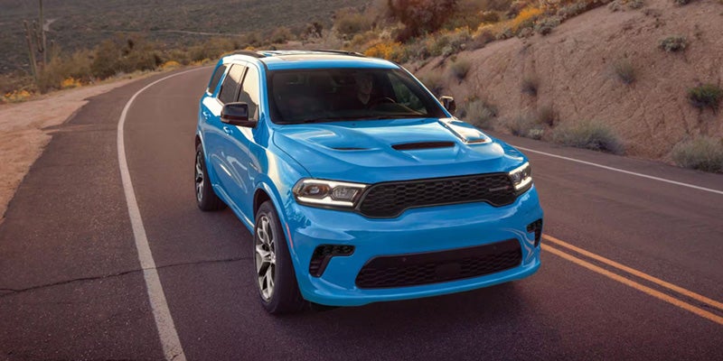 A blue Dodge Durango SUV parked on a winding road with desert landscape in the background.