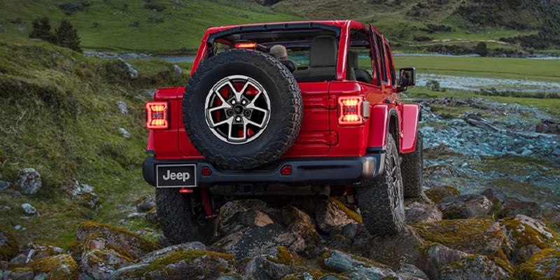 Rear view of red Jeep Wrangler crossing shallow stream