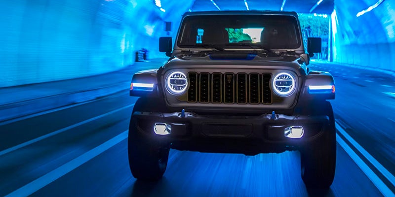 Jeep Wrangler 4xe with bright headlights driving through blue-lit tunnel