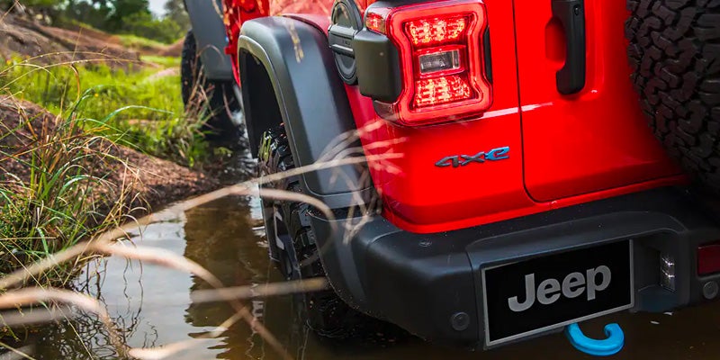 Rear view of red Jeep Wrangler 4xe driving through shallow water