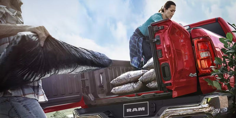 A person loading bags into the bed of a red RAM truck, while another person lifts a bag from the side.