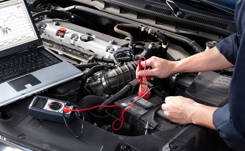 Technician testing a car battery using diagnostic equipment under the hood.